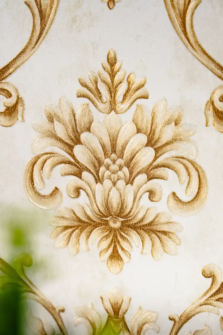 Close-up of embossed gold damask motif showing detailed floral and scroll work on cream wallpaper