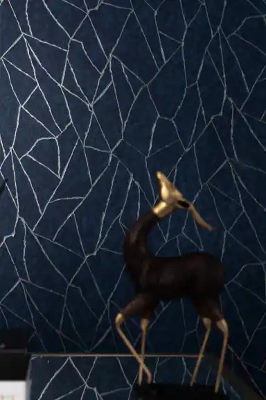 Navy blue abstract lines wallpaper installed on wall with silver geometric crack pattern and brass deer figurine