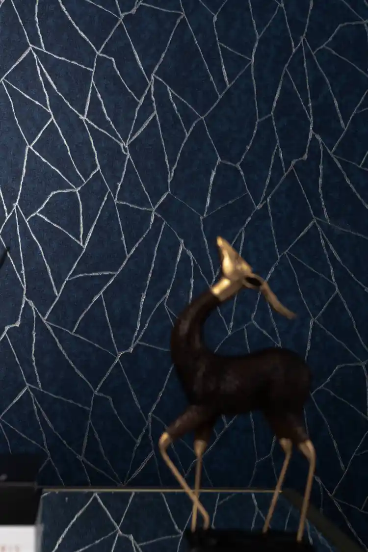 Navy blue abstract lines wallpaper installed on wall with silver geometric crack pattern and brass deer figurine