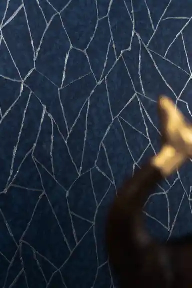 Close-up of navy wallpaper with silver crackle lines and blurred brass figurine in foreground