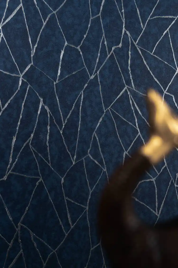 Close-up of navy wallpaper with silver crackle lines and blurred brass figurine in foreground