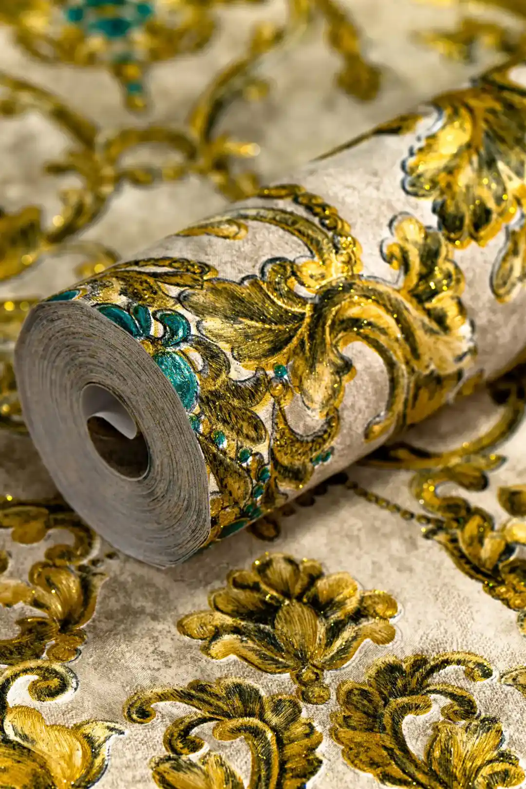 Rolled wallpaper showing ornate gold damask pattern with turquoise gem details on aged cream background