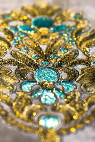 Macro shot of sparkling turquoise gem and gold glitter detailing on baroque wallpaper motif