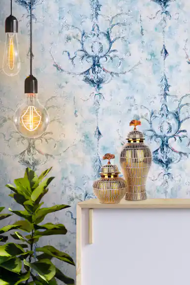 Vintage blue damask wallpaper installed behind white shelf with decorative vases and Edison bulb lights