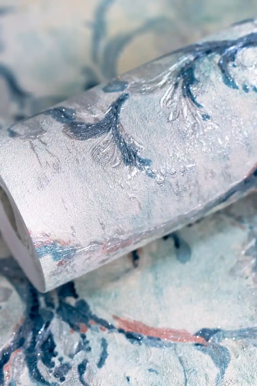 Close-up of rolled blue vintage damask wallpaper showing watercolour-effect pattern on light background