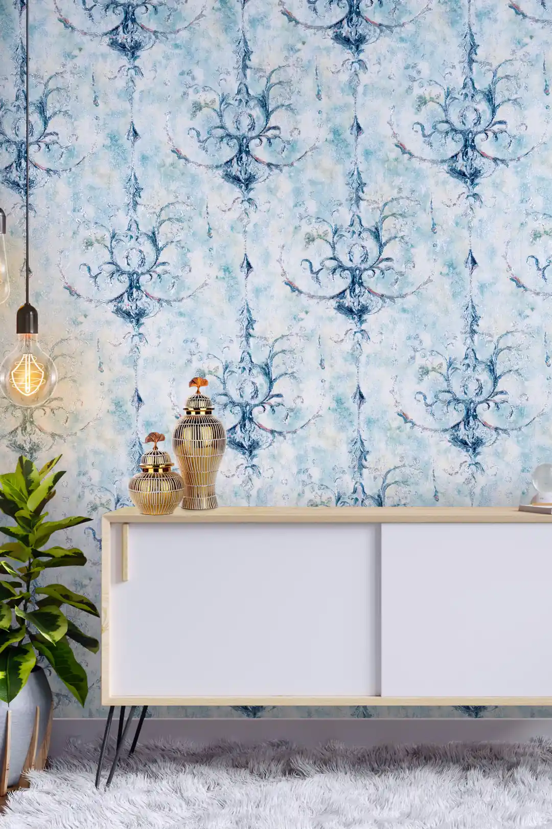 Room scene with blue textured damask wallpaper behind white sideboard, brass vases, and green plant
