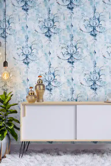 Room scene with blue textured damask wallpaper behind white sideboard, brass vases, and green plant