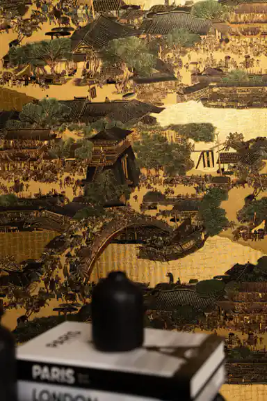 Installed golden village mural showing intricate bridge, rooftops, and marketplace scene with books on shelf