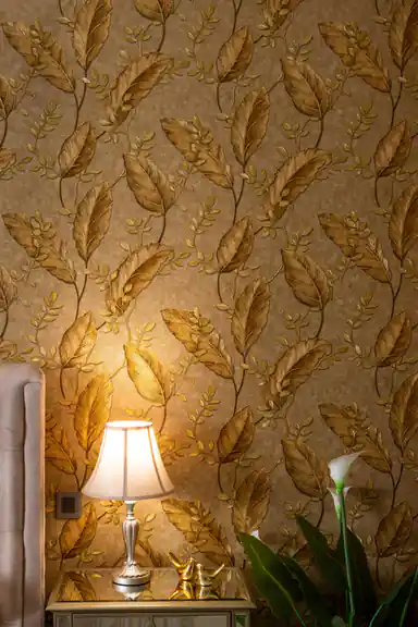 Room scene with golden tropical leaf wallpaper behind bedside lamp, golden bird figurines, and calla lily