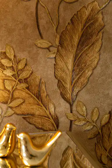Close-up of embossed golden tropical leaf and small branch detail on textured warm-toned wallpaper