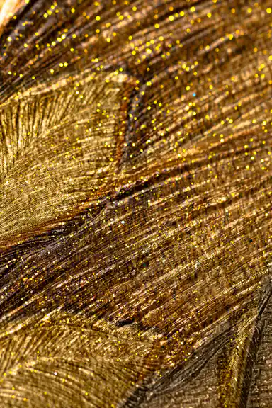 Extreme macro of golden glitter particles on embossed tropical leaf wallpaper surface texture