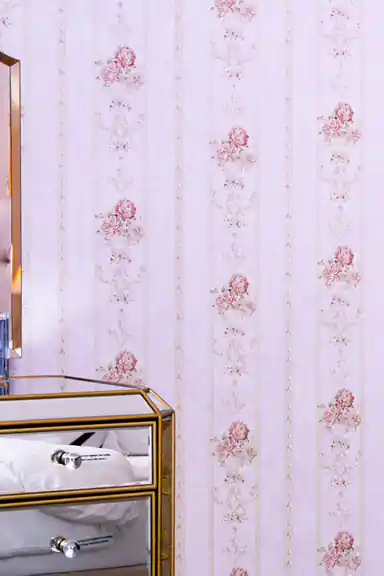 Installed pink striped wallpaper with rose motifs behind mirrored nightstand in elegant bedroom setting