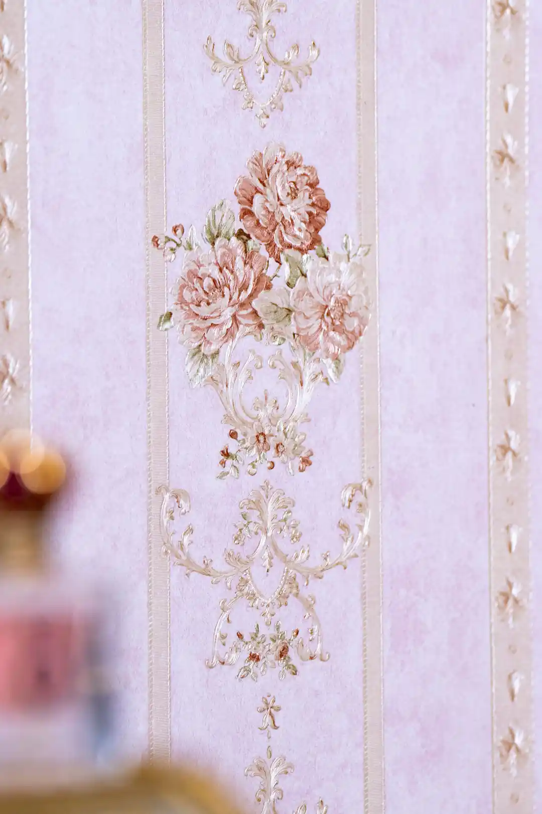 Close-up of embossed pink rose bouquet with ornate scroll detail between vertical stripes on wallpaper