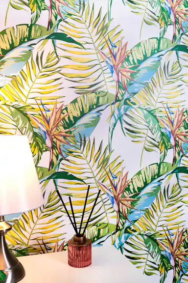Installed tropical paradise wallpaper with palm fronds behind table lamp and reed diffuser
