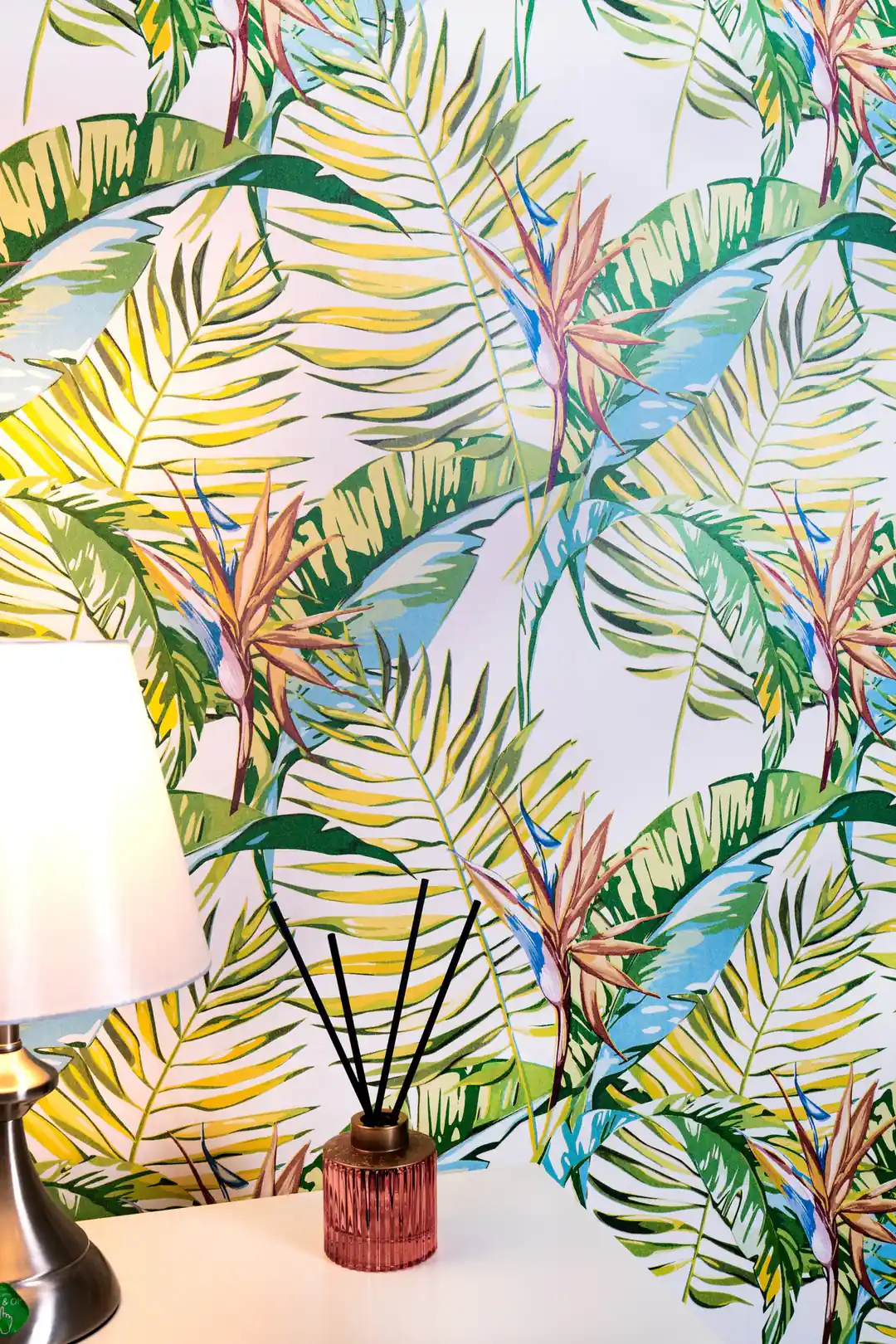 Installed tropical paradise wallpaper with palm fronds behind table lamp and reed diffuser