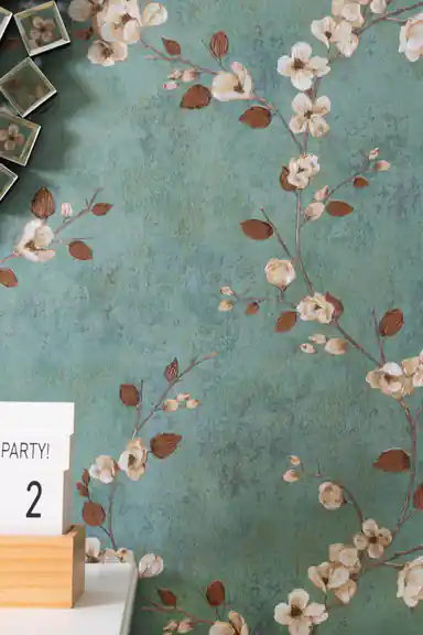 Installed teal floral branch wallpaper with magnolia blooms behind side table and reed diffuser