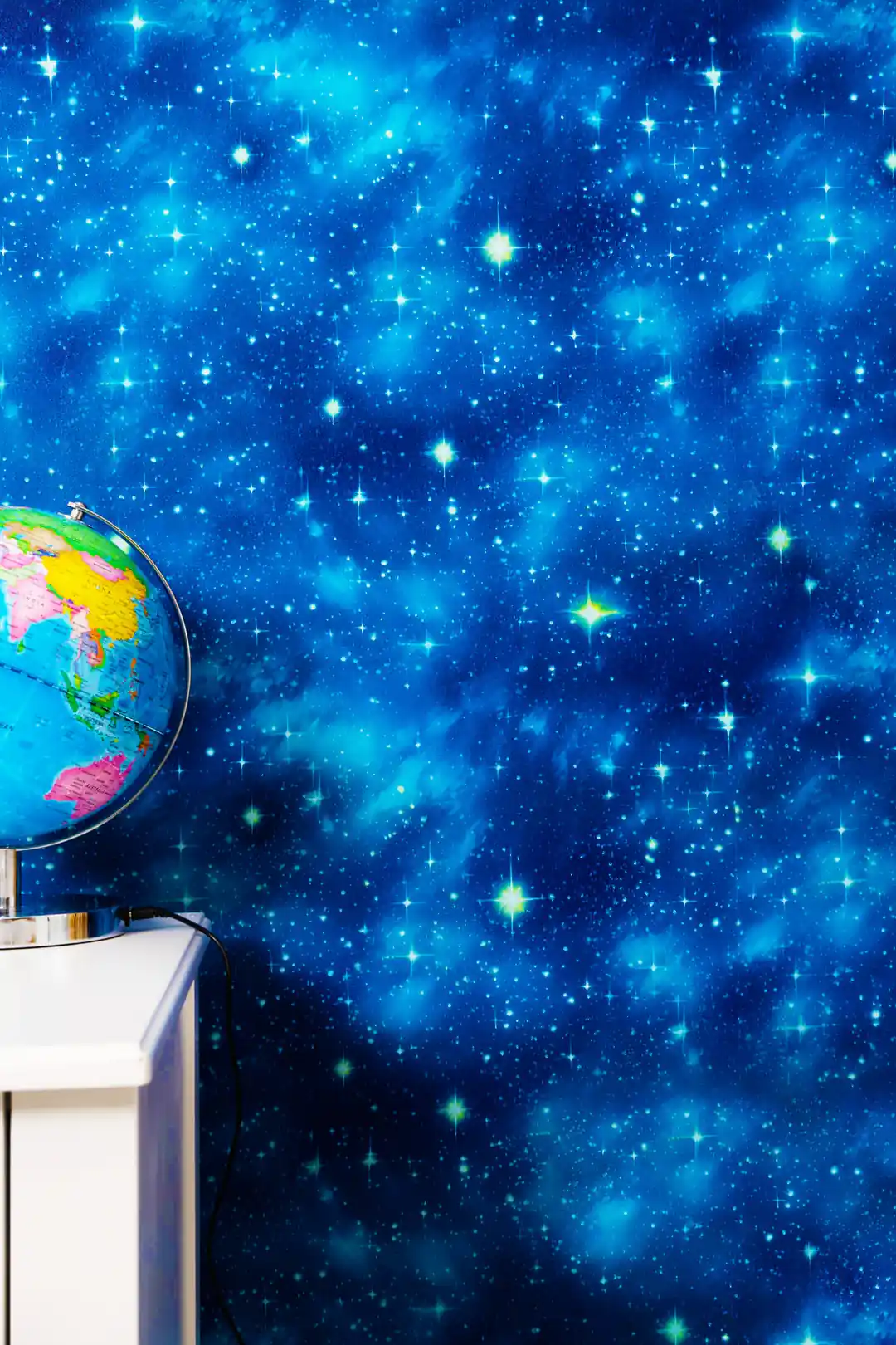 Blue galaxy wallpaper with twinkling stars behind a globe on white shelf in study room