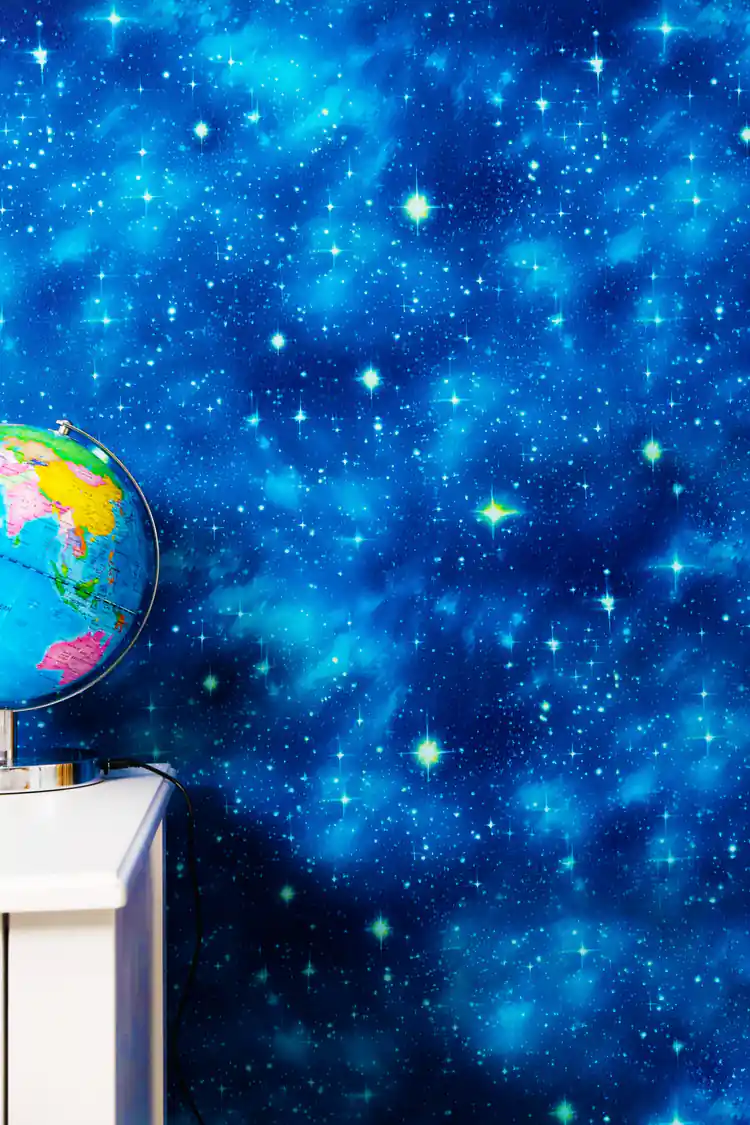 Blue galaxy wallpaper with twinkling stars behind a globe on white shelf in study room
