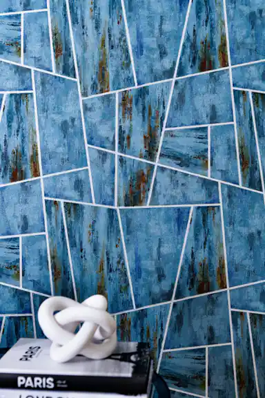 Teal geometric panels wallpaper installed on wall with white decorative knot sculpture on stacked Paris and London books