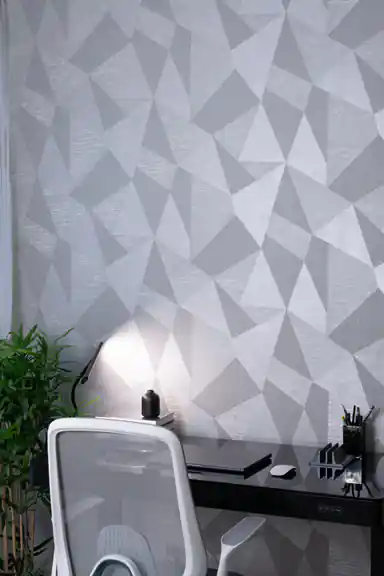 Installed grey 3D triangle wallpaper in a modern office with dark desk, white office chair, desk lamp, and green plant