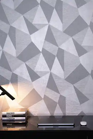Grey 3D geometric wallpaper behind a dark desk with black desk lamp and stacked books