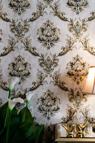 Vintage damask wallpaper with gold scroll pattern on cream base behind tropical plant leaves and gold decor