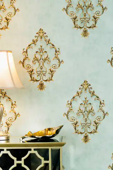 Elegant sage green wallpaper with gold damask motifs behind table lamp and gold decorative bowl