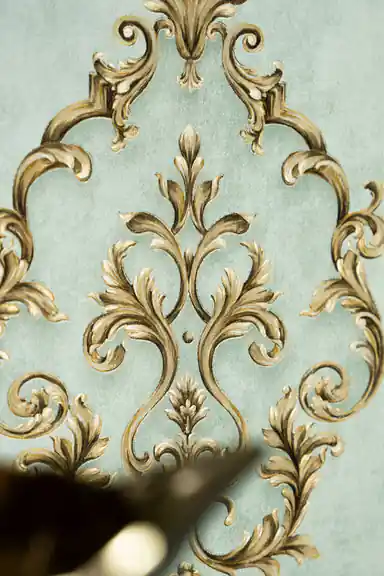 Close-up of single gold baroque scroll motif on sage green textured wallpaper background