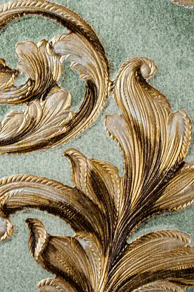 Extreme macro of gold embossed acanthus leaf scroll detail showing raised metallic texture
