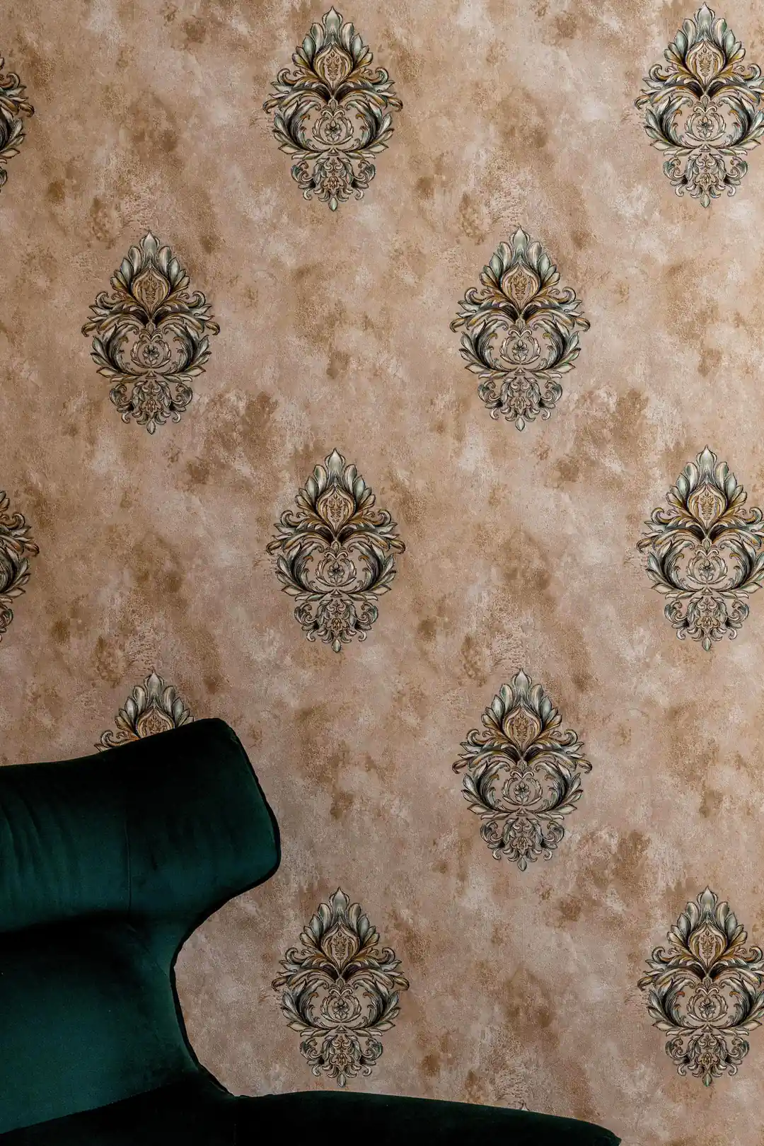 Ornate damask motif wallpaper behind dark green velvet sofa in elegant room setting