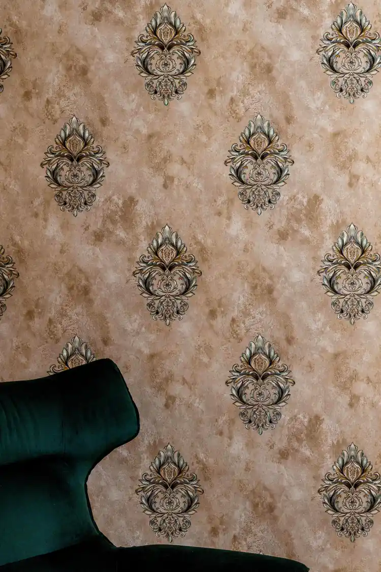 Ornate damask motif wallpaper behind dark green velvet sofa in elegant room setting