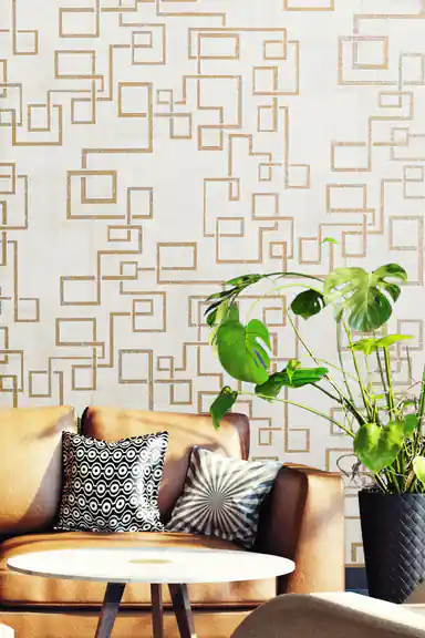 Gold maze pattern wallpaper in living room with tan leather sofa, monstera plant and round table