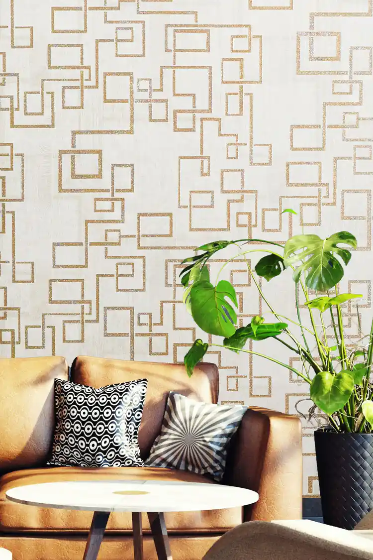 Gold maze pattern wallpaper in living room with tan leather sofa, monstera plant and round table