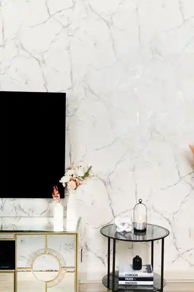 White marble wallpaper in living room with TV on mirrored console, flowers and glass side table