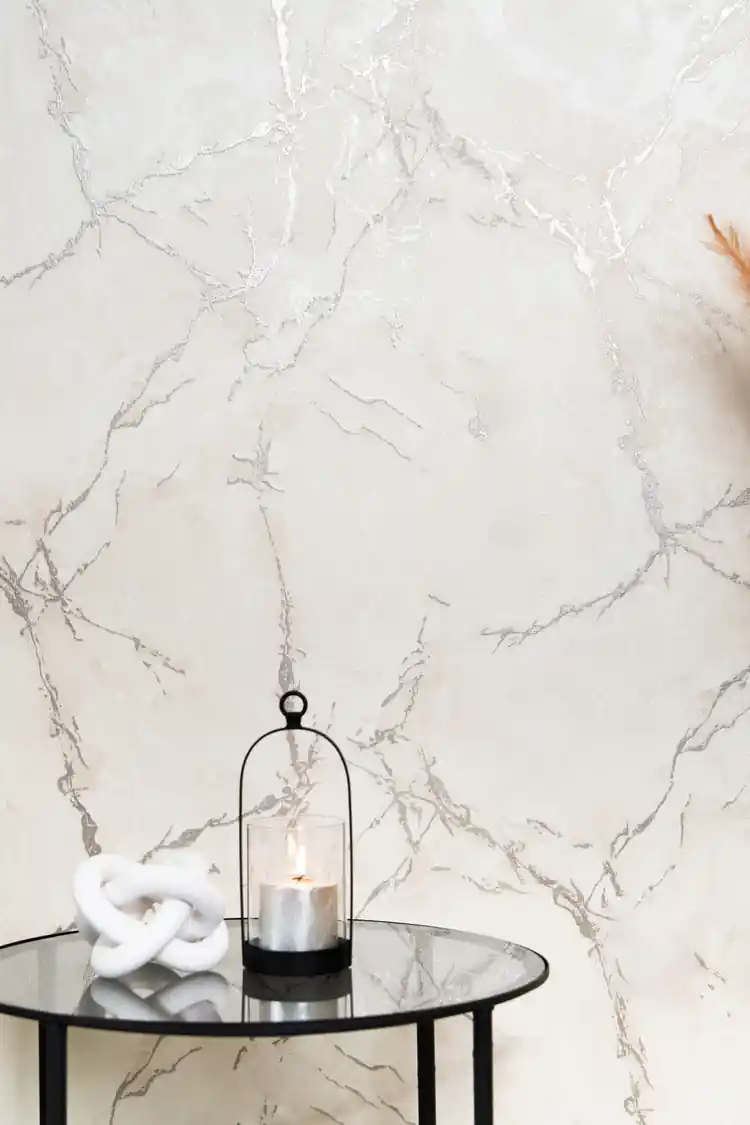 Carrara marble wallpaper with silver veins behind glass side table with lantern candle and white chain-link sculpture