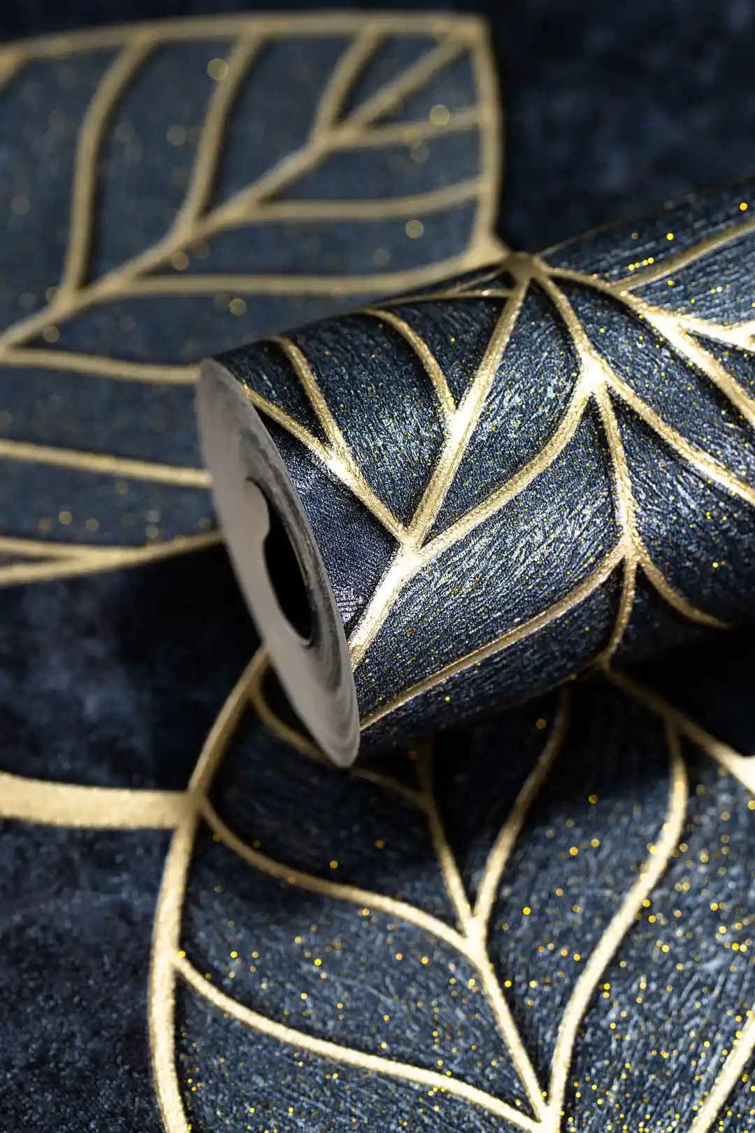 Midnight blue gold leaf wallpaper roll showing embossed leaf veins on dark textured base