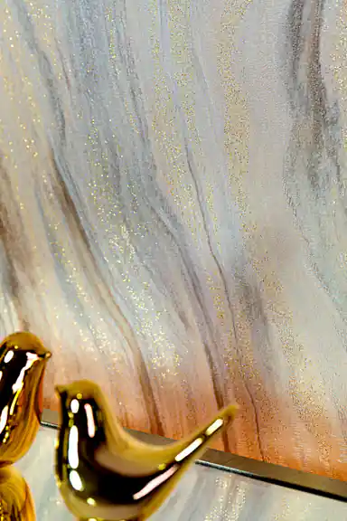 Close-up of marble wave wallpaper with gold glitter veins behind gold bird figurine on shelf