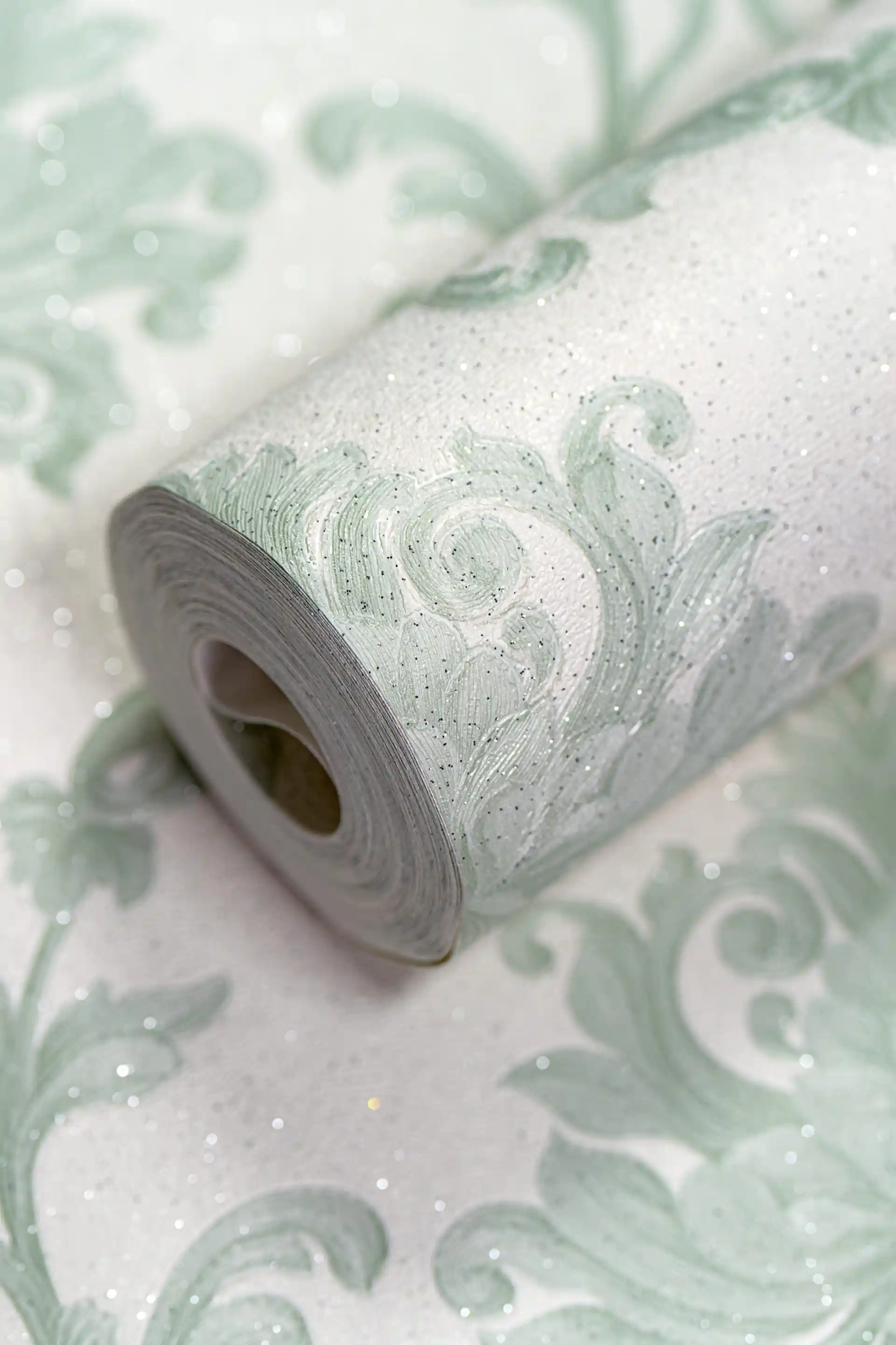Sage green damask wallpaper roll with embossed floral scroll pattern and sparkling glitter accents