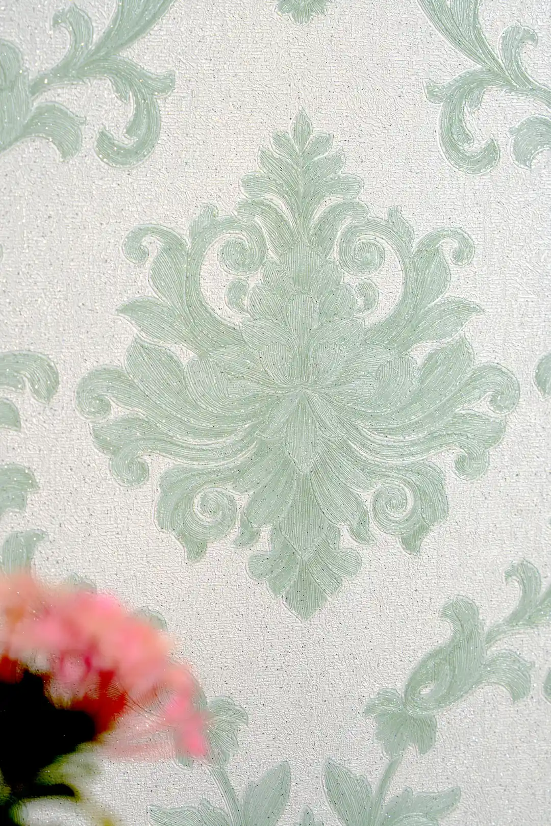 Detailed view of a single embossed sage green damask medallion with a pink flower in the foreground