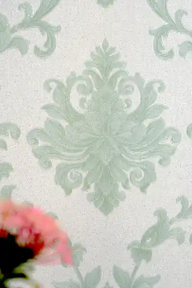 Detailed view of a single embossed sage green damask medallion with a pink flower in the foreground