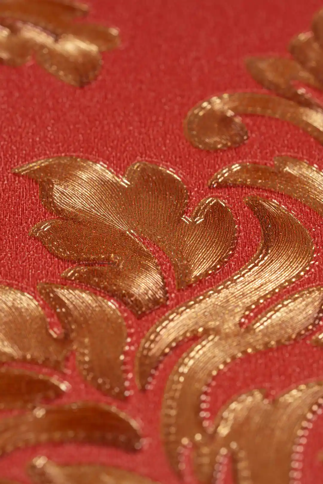 Close-up macro of the embossed golden leaf motif showing metallic sheen on the deep red background