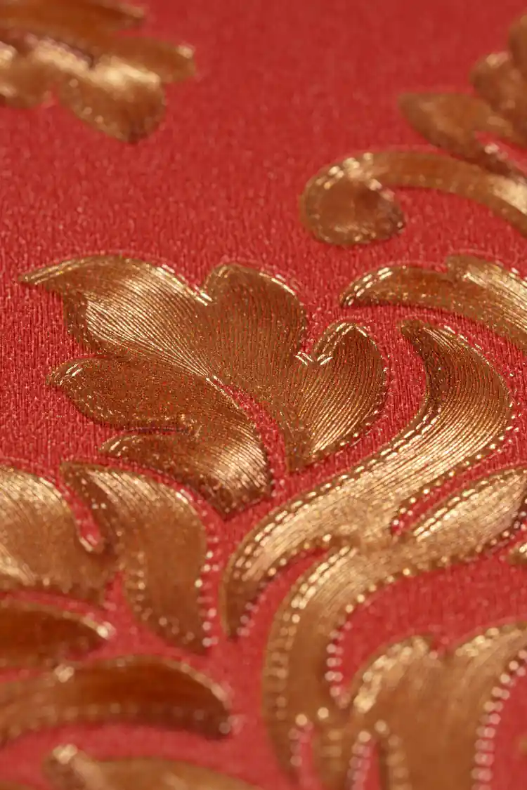 Close-up macro of the embossed golden leaf motif showing metallic sheen on the deep red background