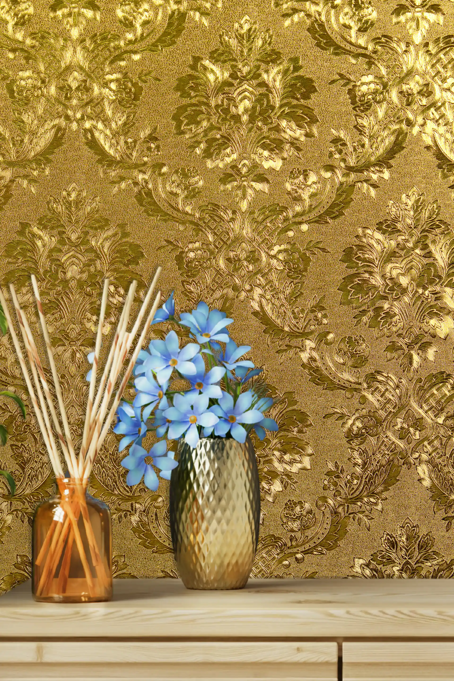 Shiny gold foil wallpaper with embossed baroque floral damask pattern displayed on a shelf with blue flowers