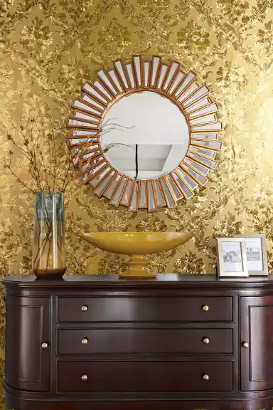 Close-up of the gold foil wallpaper roll revealing embossed baroque scroll detail and metallic sheen