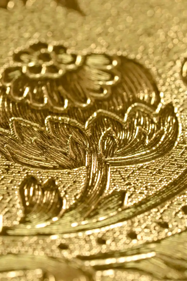 Extreme macro detail of the embossed gold baroque pattern showing intricate flower and leaf engraving