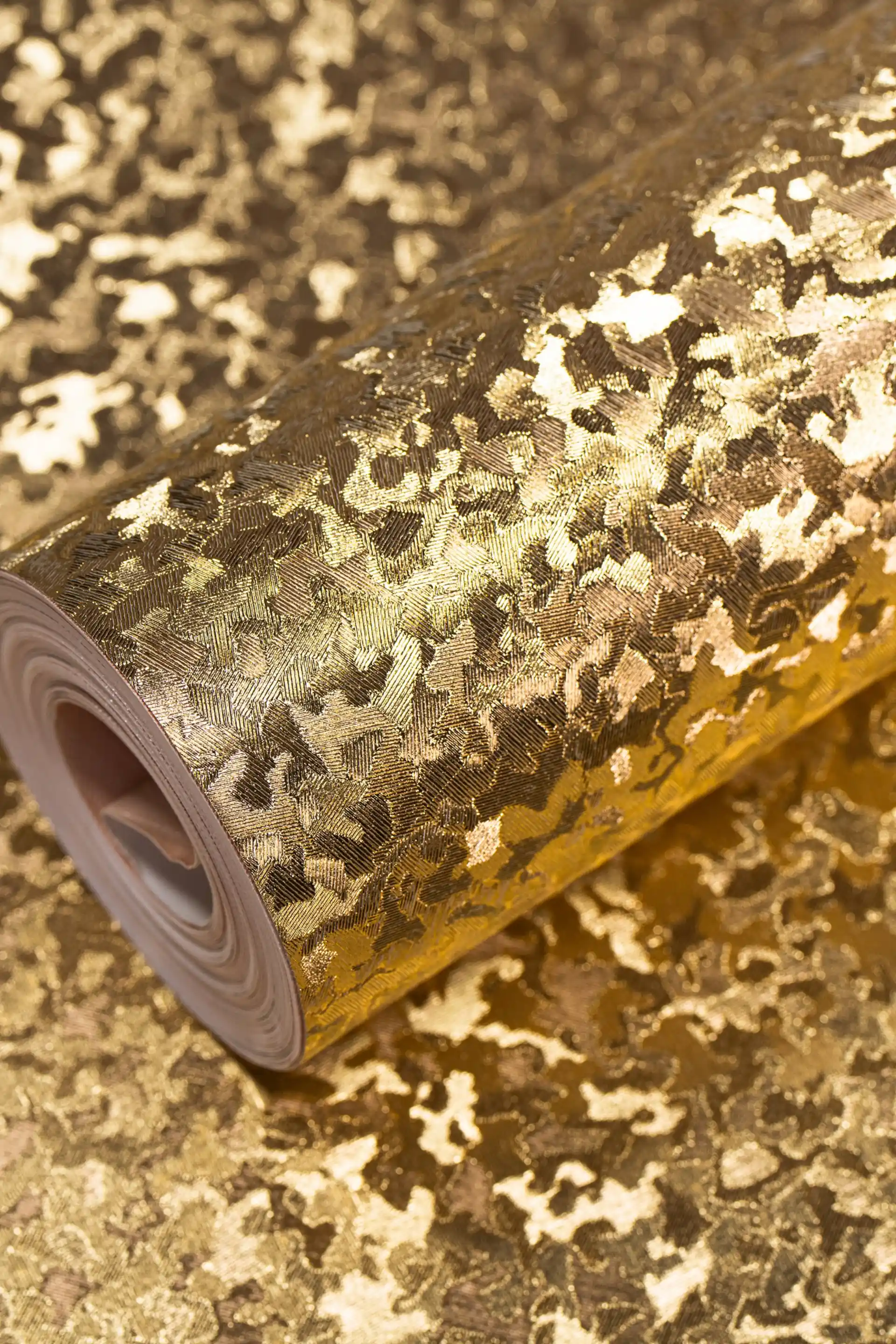 Luxe metallic gold leaf flake foil wallpaper roll with abstract crackled texture on a reflective surface
