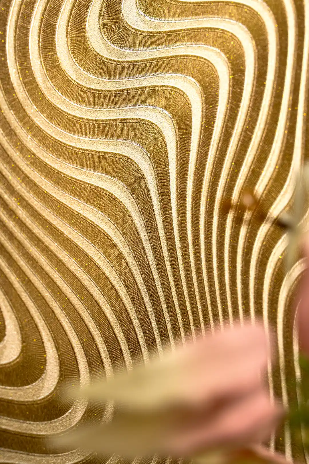 Close-up of the embossed gold wavy curves with blurred pink flowers in the foreground