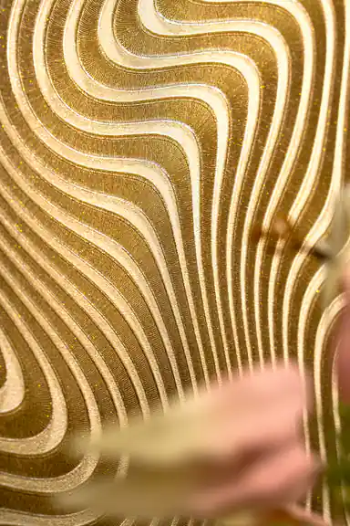 Close-up of the embossed gold wavy curves with blurred pink flowers in the foreground