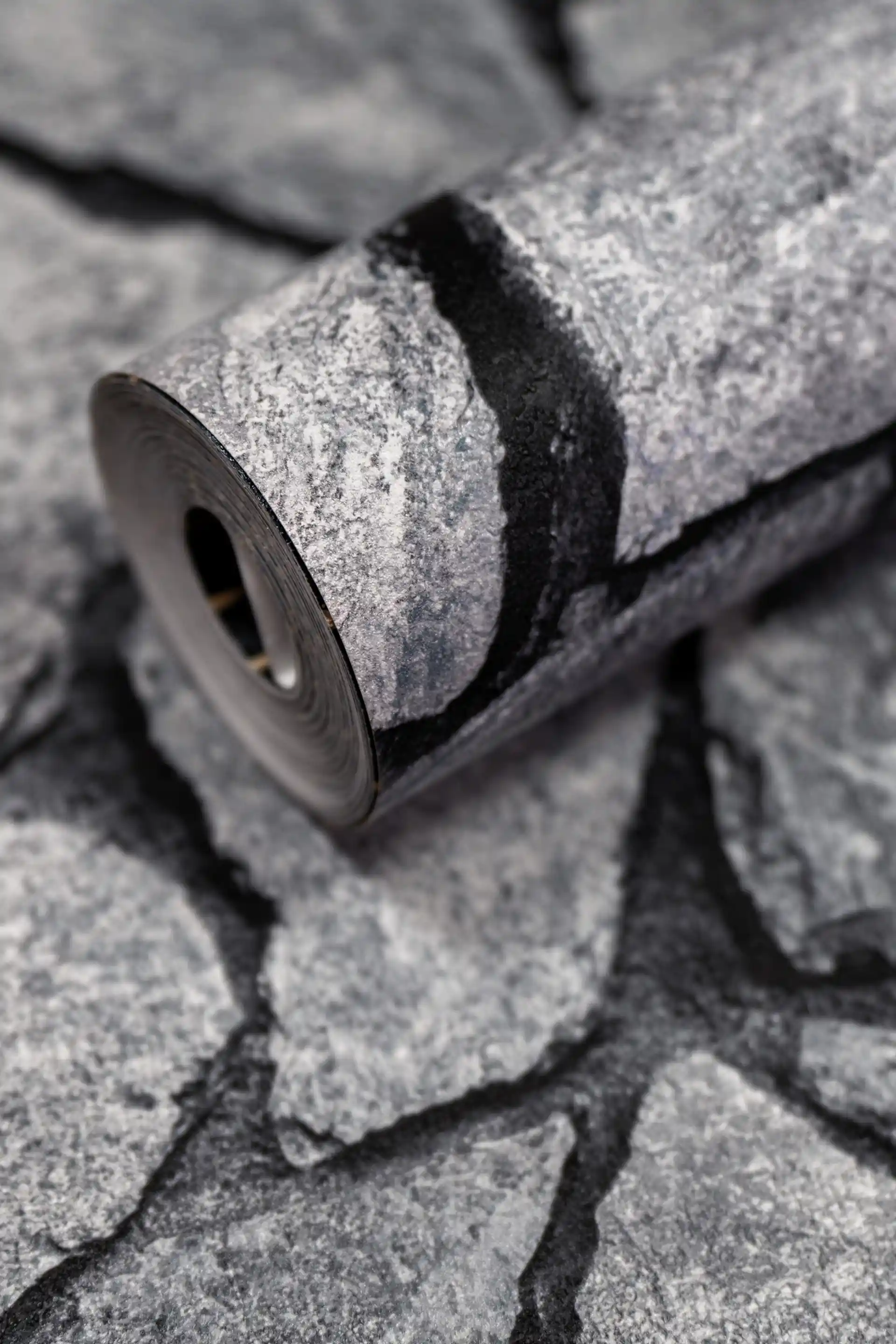 Dark grey stacked stone wallpaper roll with realistic cracked slate texture on a matte finish