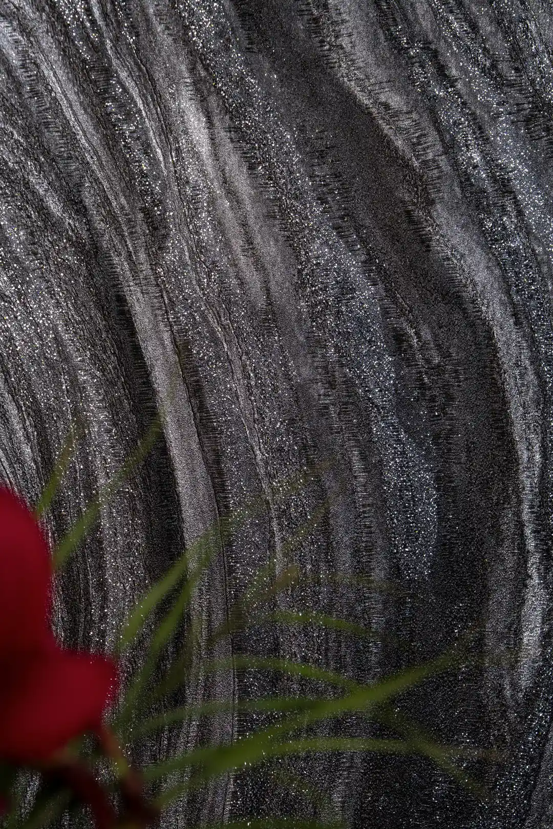 Close-up of silver glitter marble wallpaper with dramatic grey swirls and a red flower in foreground
